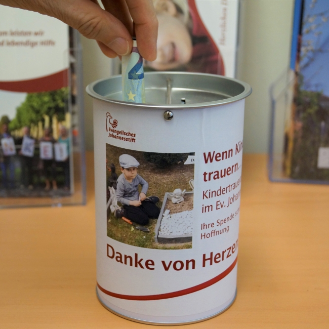 Eine Hand steckt einen 20-Euro-Schein in eine Spendendose.