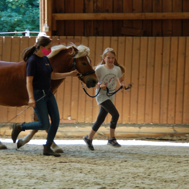 Eine Trainerin und ein Kind führen ein Pferd.