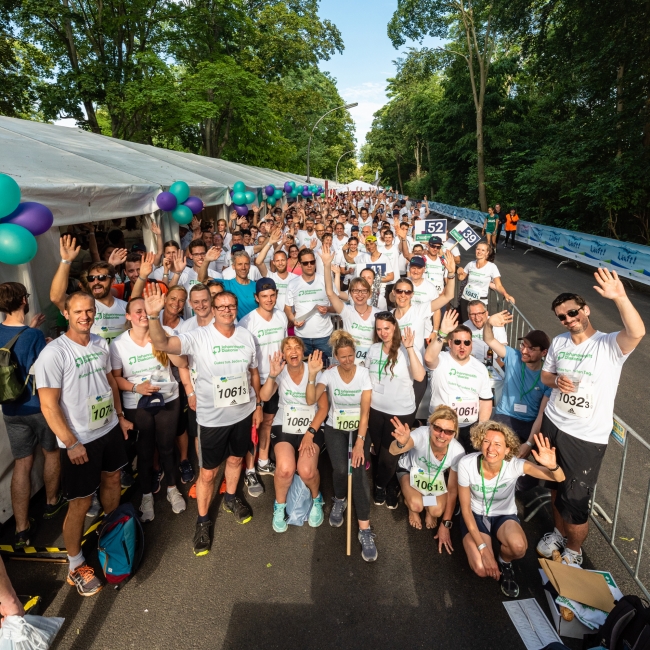Viele Mitarbeiterinnen und Mitarbeiter mit Laufshirt stehen eng nebeneinander und freuen sich auf den Staffellauf.