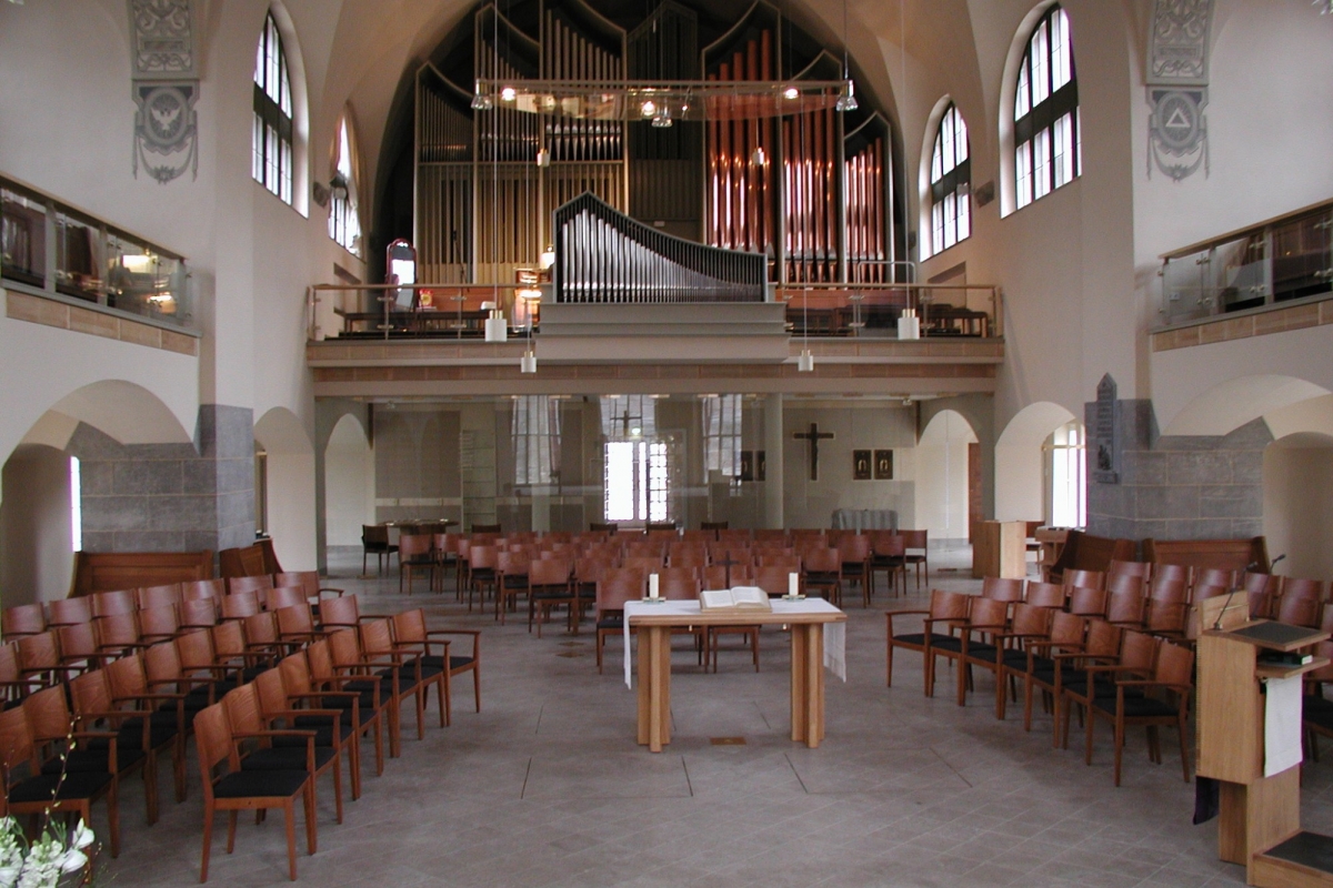 Innenraum der der Stiftskantorei mit Blick auf die Orgel. Frontal, links und rechts sind Stuhlreihen zu sehen.