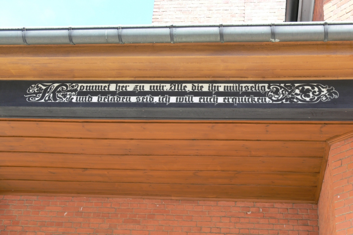 Ein Spruchband mit Bibelzitat auf Holz am Dach der Loggia der Stiftskantorei.