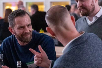 Drei Personen auf einer Party schauen sich etwas auf einem Handy an