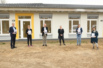 Vier Frauen und zwei Männer stehen vor der Schule ohne Grenzen und halten in ihren Händen das pädagogische Konzept der Schule.